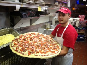 Cook holding XXL pizza with bacon at Pino's Pizza