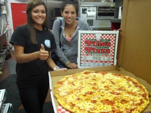 two woman holding an XXL pizza from Pino's Pizza in oc