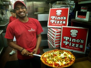 man holding cooked Pino's Pizza in kitchen