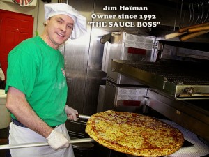 Jim Hofman of Pino's Pizza holding an extra large pizza in oven