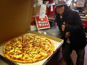 man in black jacket giving thumbs up next to jumbo sized Pino's Pizza
