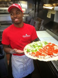 Pino's Pizza employee holding a raw half peppers and pepperoni pizza in kitchen at Pino's Pizza OC